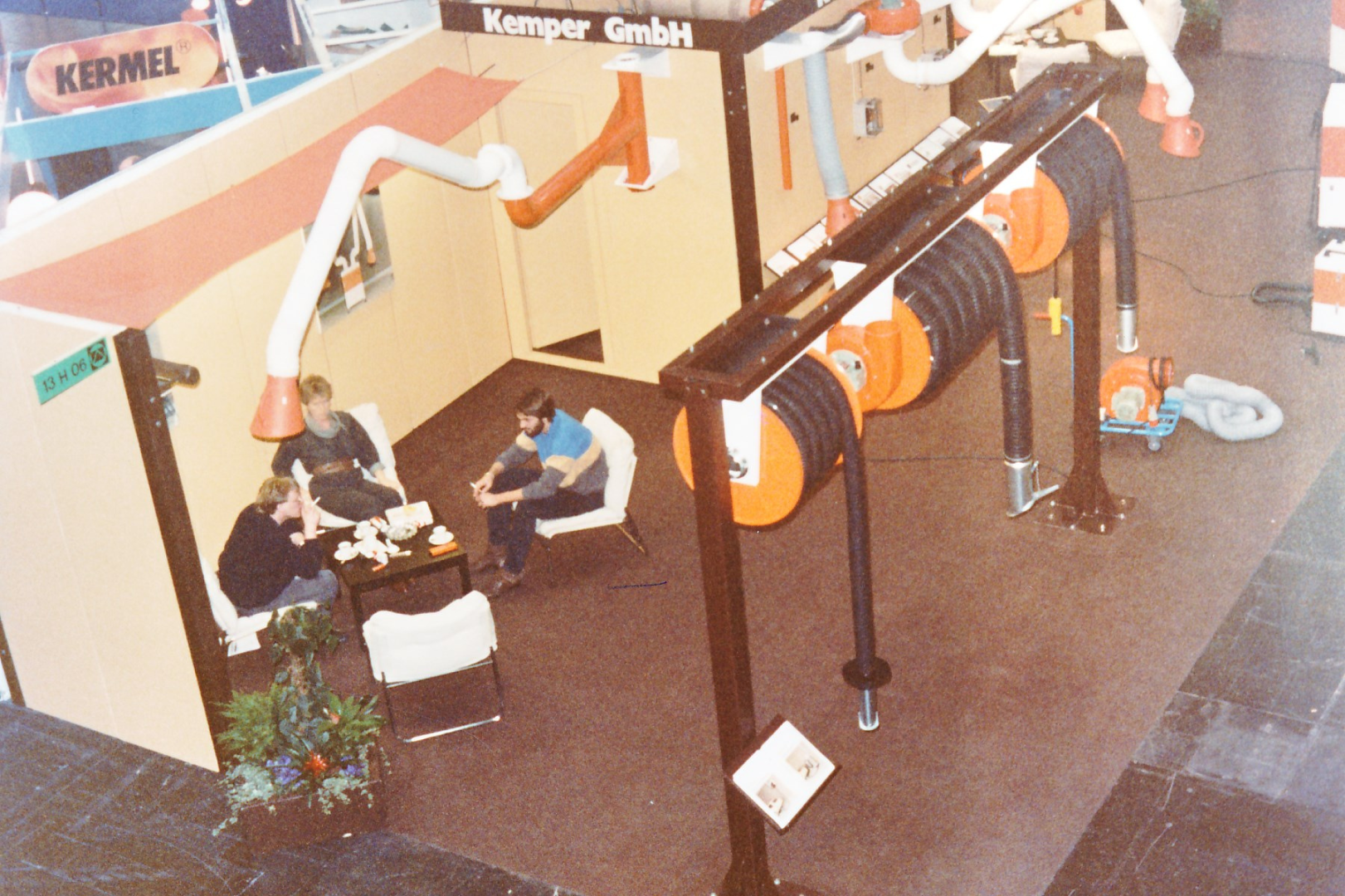 Kemper GmbH trade fair booth showcasing extraction systems, hose reels and visitors in a discussion area.