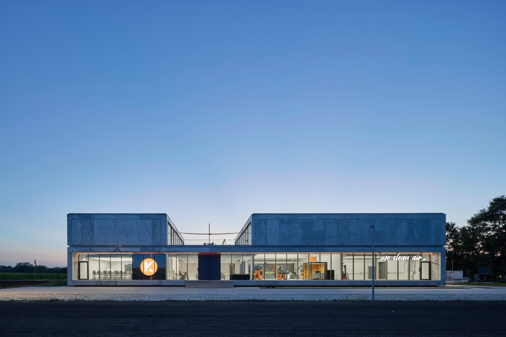 Modern company building with a large glass facade, illuminated interior spaces and visible work areas at dusk.