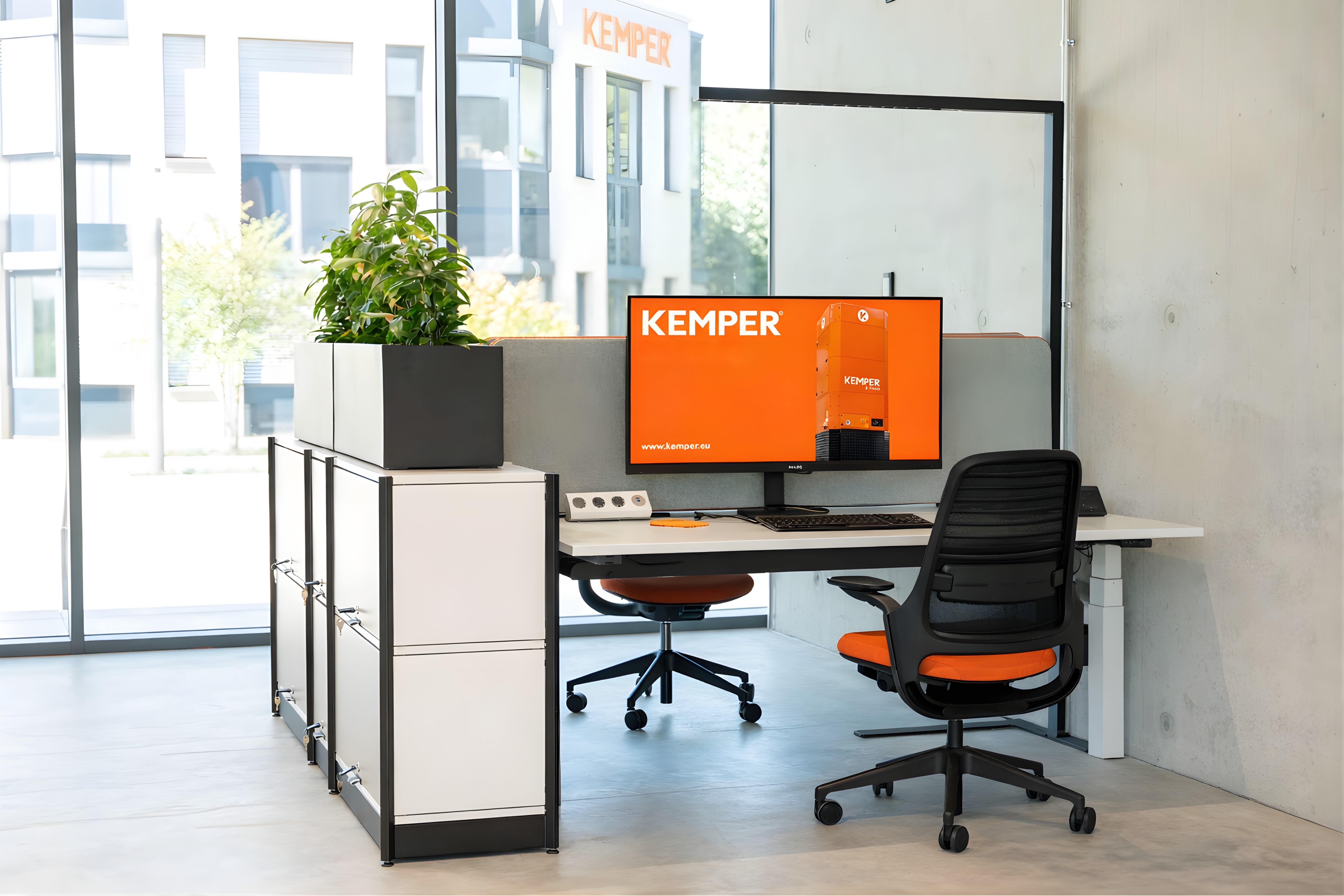 Bright modern office workspace with desk, monitor displaying a KEMPER product and ergonomic office chair