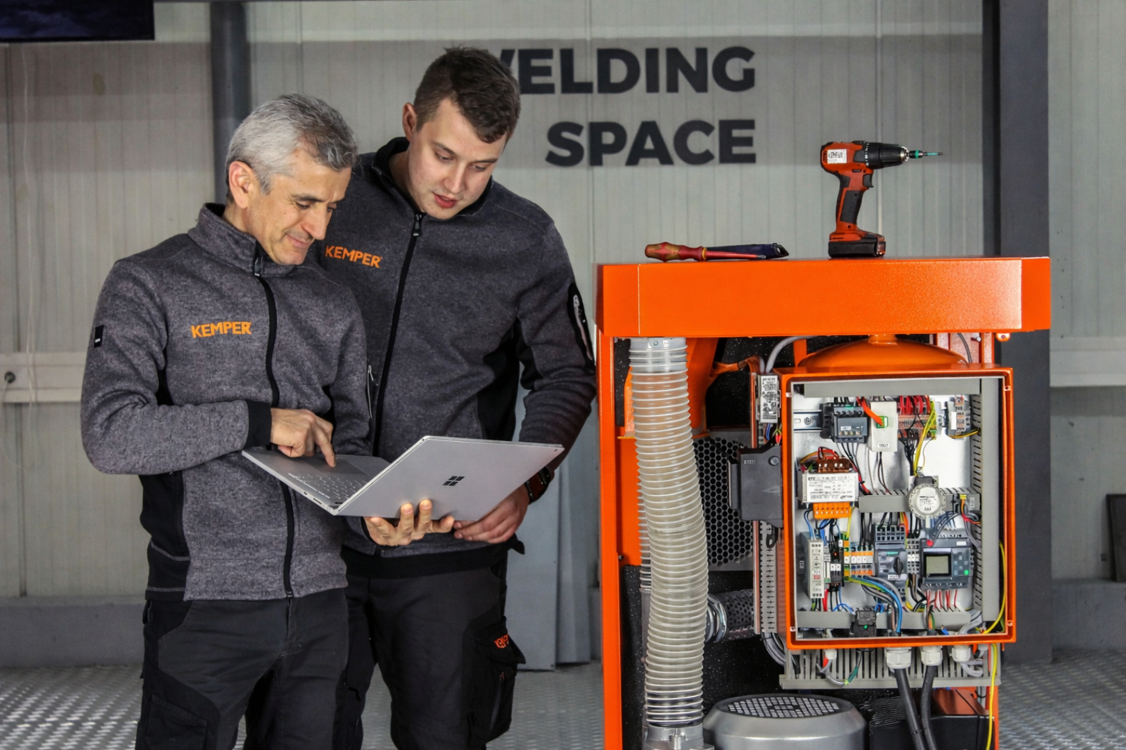 Two KEMPER service technicians analysing system data on a laptop next to an open industrial extraction and control unit.