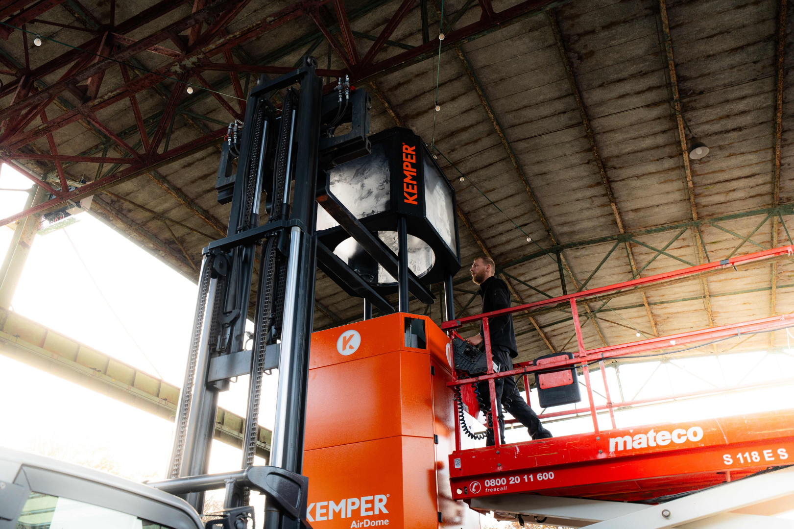 Technician installing a large extraction system in an industrial hall using an elevated work platform.