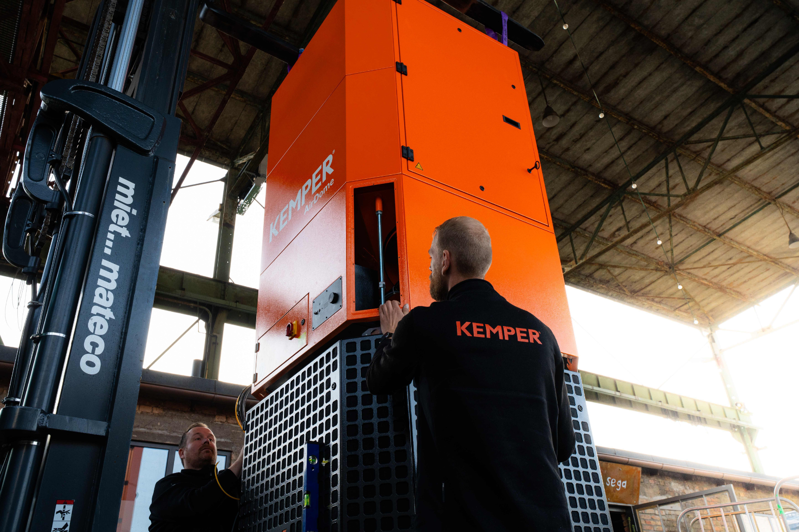 KEMPER service technicians performing maintenance on a large industrial extraction and filtration system inside a production facility.