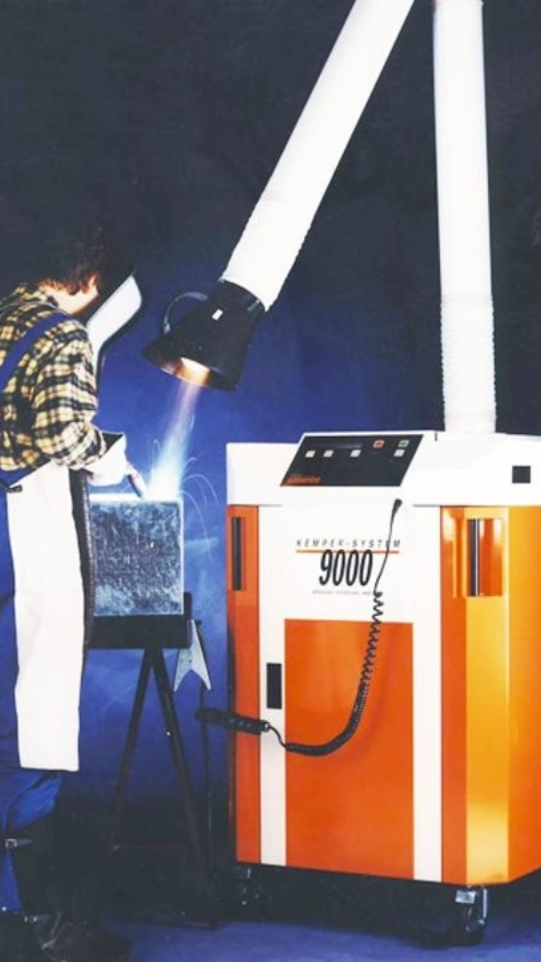 Worker welding with a stationary extraction unit and extraction arm capturing welding fumes directly at the source.