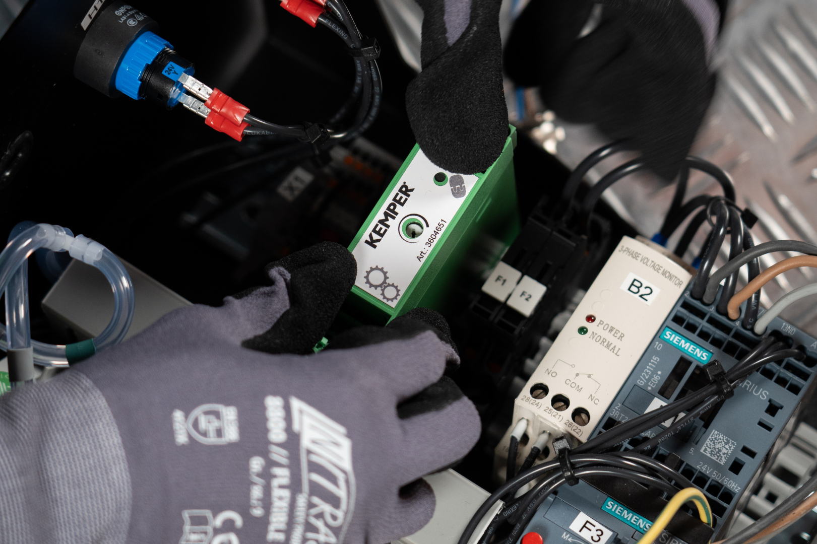 Service technician installing a KEMPER sensor module inside an electrical control cabinet with electronic components.