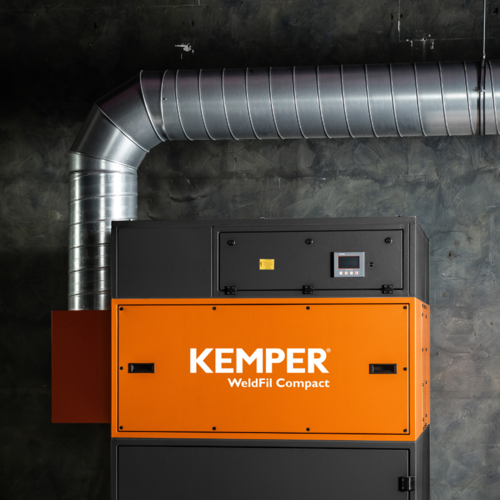 Orange-schwarzes KEMPER WeldFil Compact Absauggerät mit angeschlossenem silbernem Lüftungsrohr, installiert vor einer dunklen Industriewand.